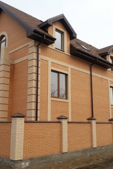 Изправена пред къщата и оградата с жълта тухла